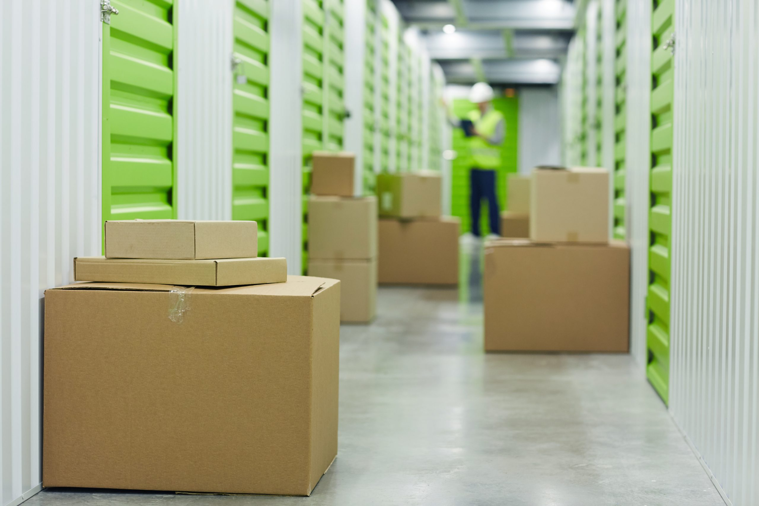 Close-up of cardboard boxes standing near the stockrooms with manual worker working in the background in warehouse