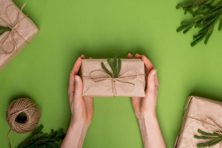 Eco present with green plants in craft paper in hands on a green background top vew